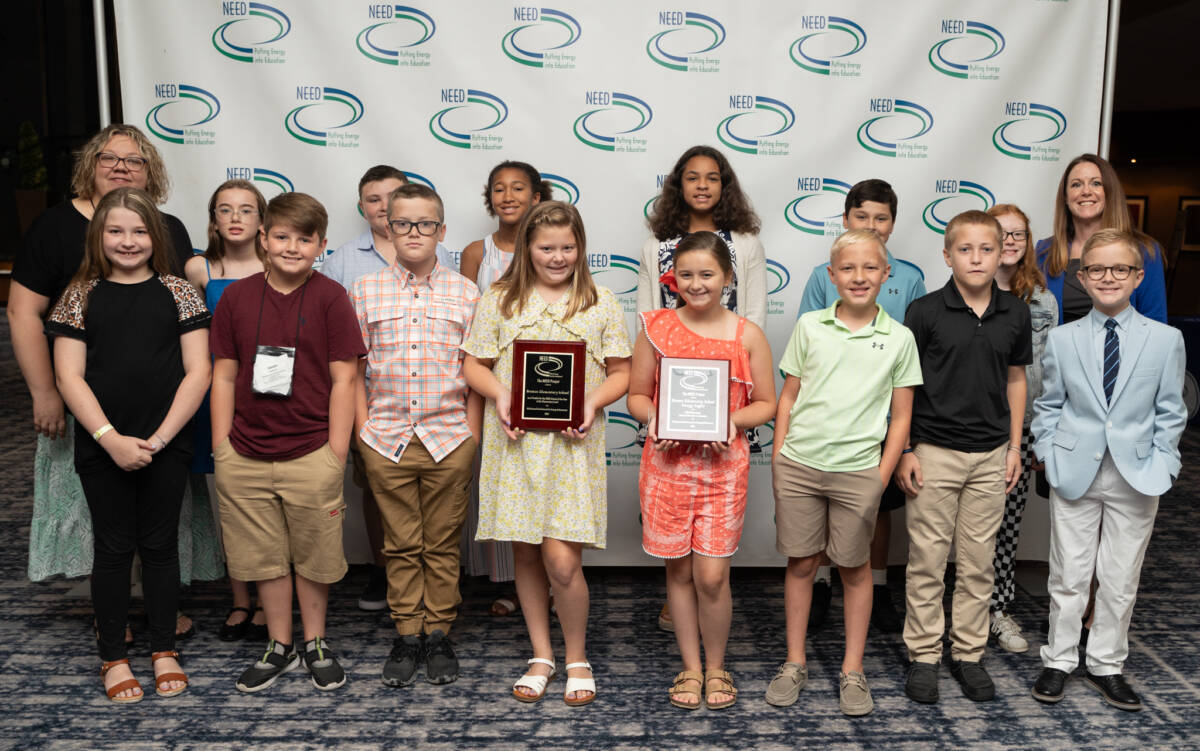 Award winner students and their teachers in front of a NEED logo backdrop