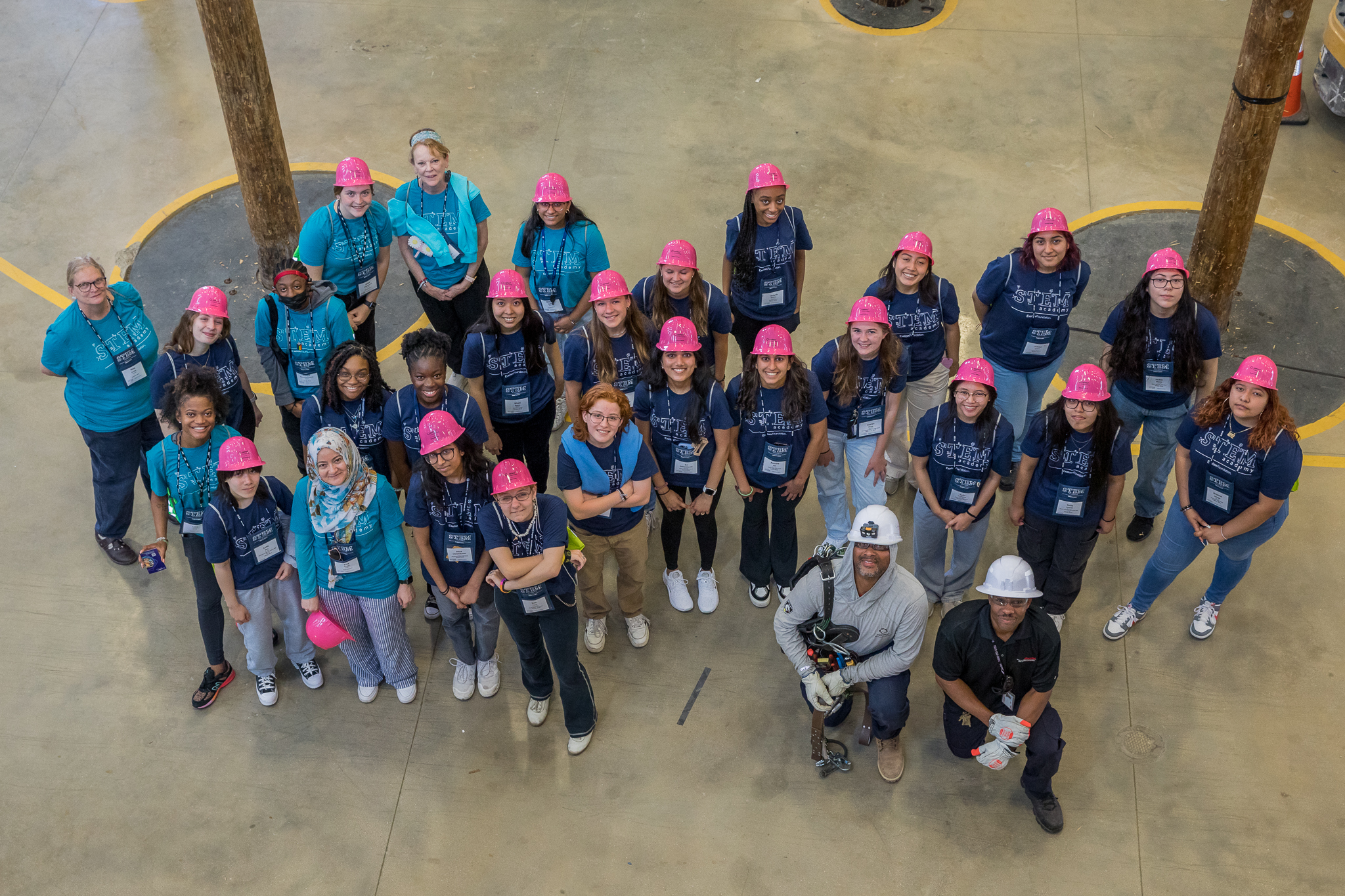 Students in pink hardhats looking up at the camera high above