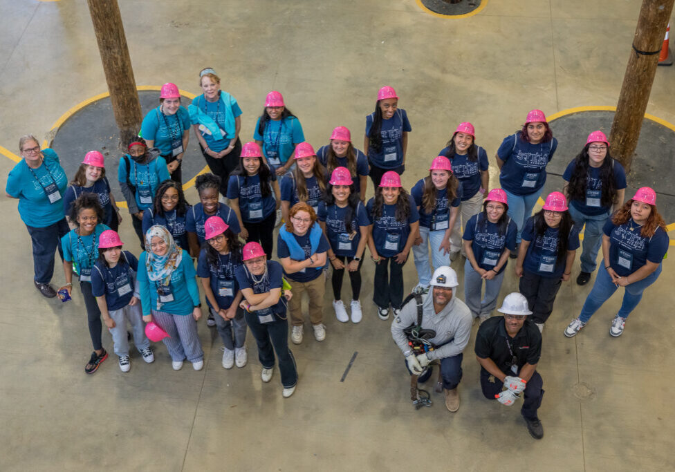 Students in pink hardhats looking up at the camera high above