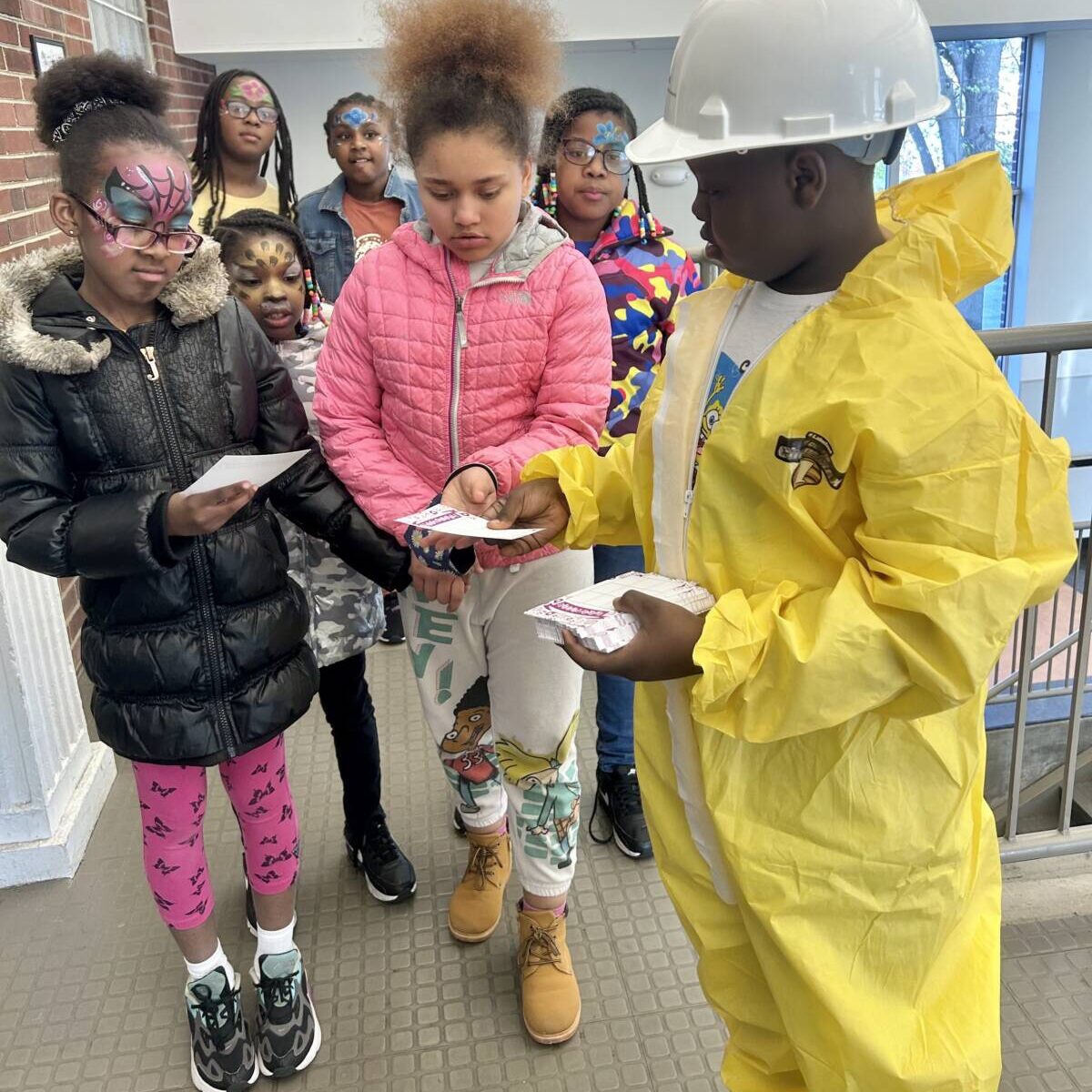 Student in a hazmat suit handing out flyers to other face painted students