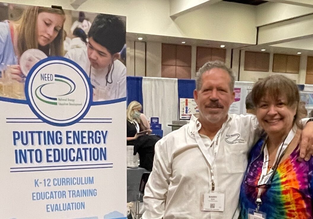 Teacher standing next to a "putting energy into education" sign